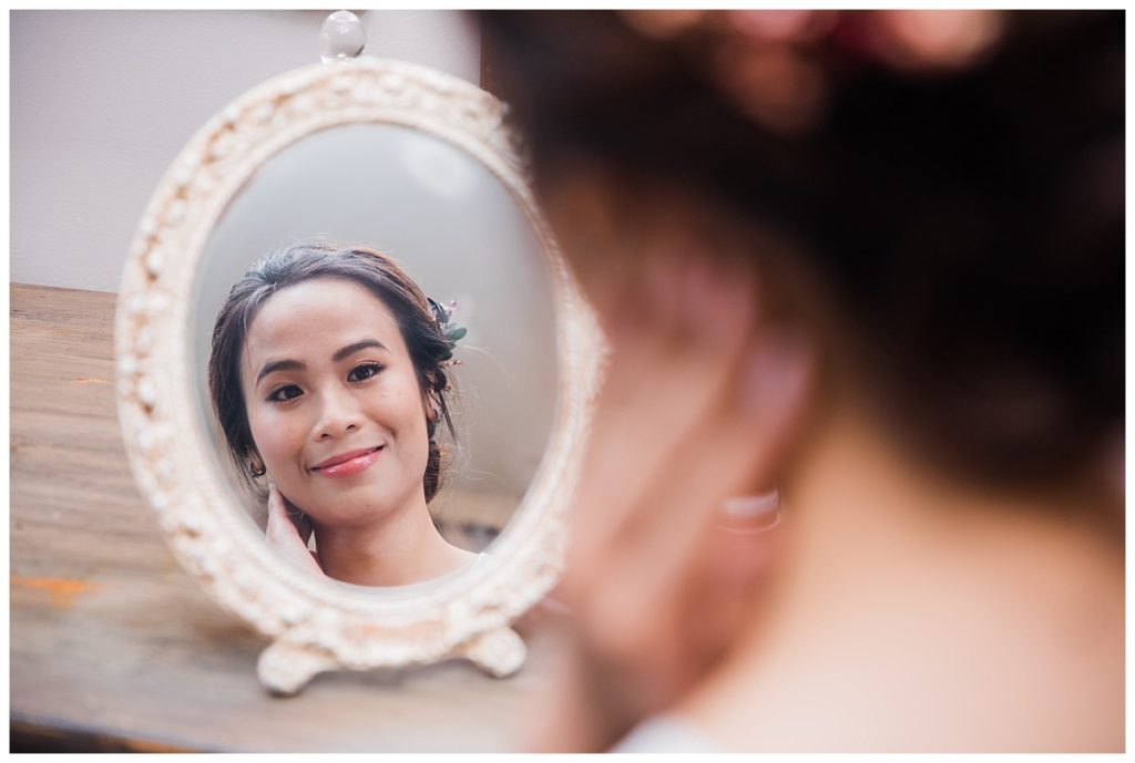Bride looking in mirror for first look of bridal makeup photographed by Picture Bouquet Studio for outdoor wedding. 
