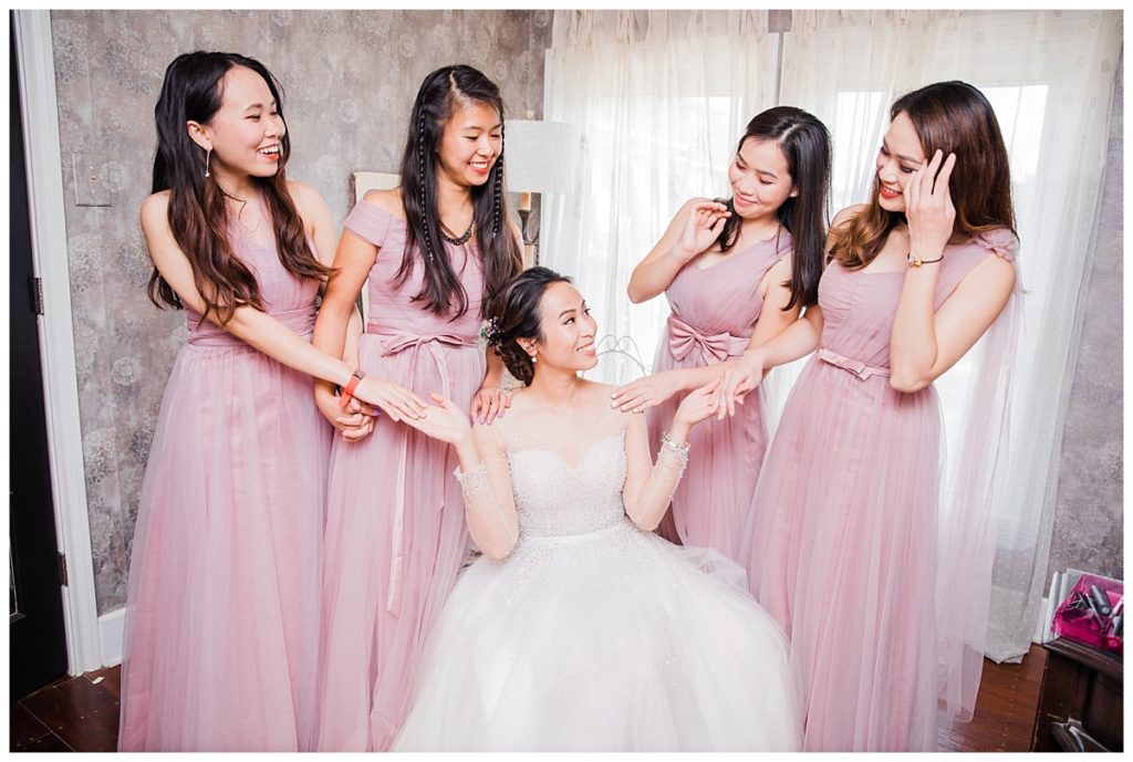 Bridesmaids in dusty pink dress holds hands with the bride in a long sleeve wedding dress during the getting ready portion of the day photographed by Dallas wedding photographer Picture Bouquet Studio. 
