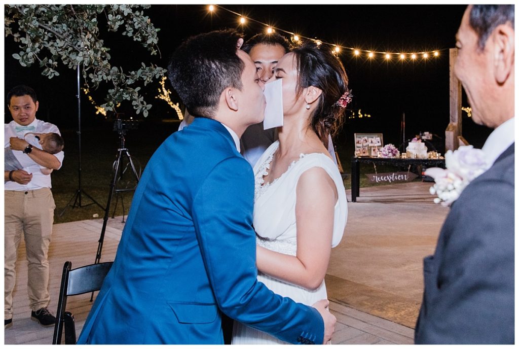 Vietnamese bride and groom play kissing for the envelope game during reception for outdoor wedding at Stonebridge Wedding Venue photographed by Dallas wedding photographer Picture Bouquet Studio. 