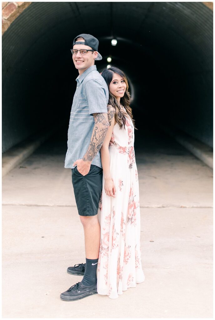 Engaged couple poses smiling in front of tunnel for an Adriatica Village engagement session photographed by Dallas wedding photographer Jenny Bui of Picture Bouquet Studio. 