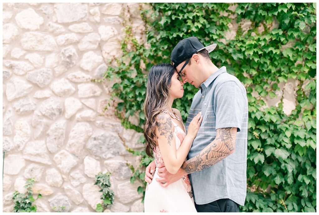 Engaged couple poses in front of vine covered wall for an Adriatica Village engagement session photographed by Dallas wedding photographer Jenny Bui of Picture Bouquet Studio. 