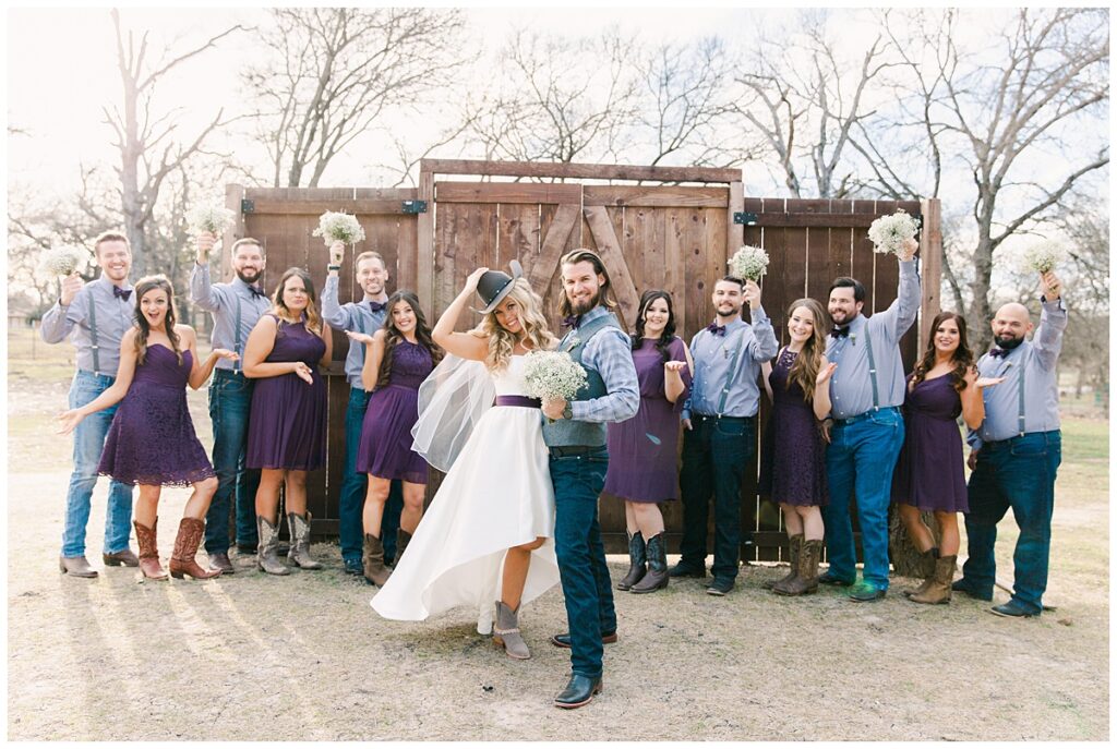 Texas styled bridal party in cowboy boots and bowties poses in front of barn door for bridal party portraits for outdoor Texas styled wedding at Fort Worth Country Memorial Wedding Venue photographed by Dallas wedding photographer Jenny Bui of Picture Bouquet Studio. 