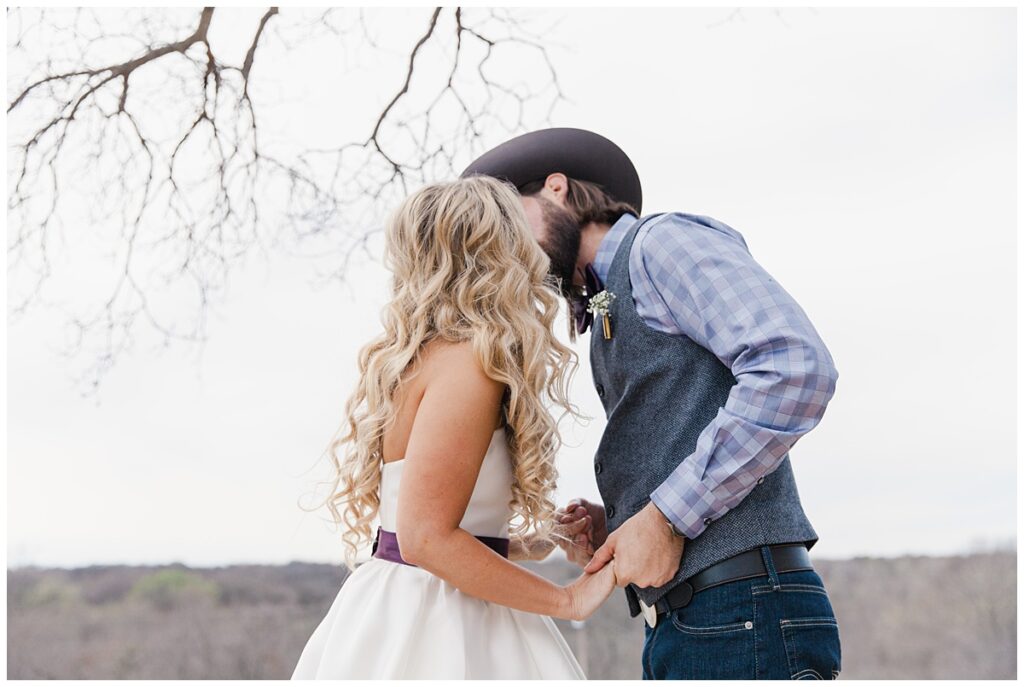 Texas styled bride and groom leans in for kiss for outdoor Texas styled wedding at Fort Worth Country Memorial Wedding Venue photographed by Dallas wedding photographer Jenny Bui of Picture Bouquet Studio. 