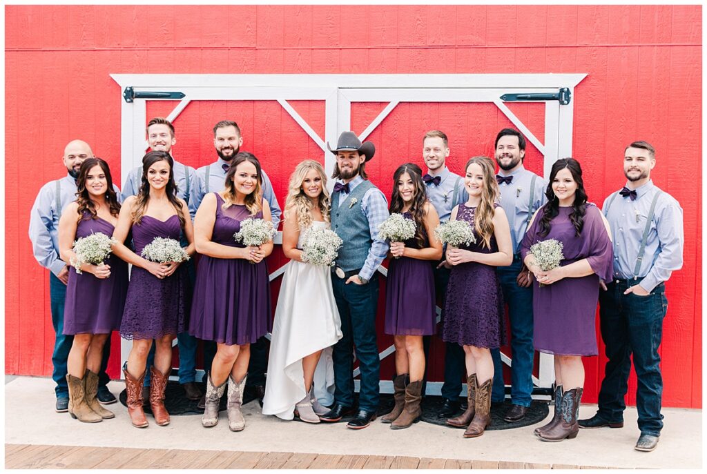 Texas styled bridal party poses with bride and groom in front of red barn for outdoor Texas styled wedding at Fort Worth Country Memorial Wedding Venue photographed by Dallas wedding photographer Jenny Bui of Picture Bouquet Studio. 