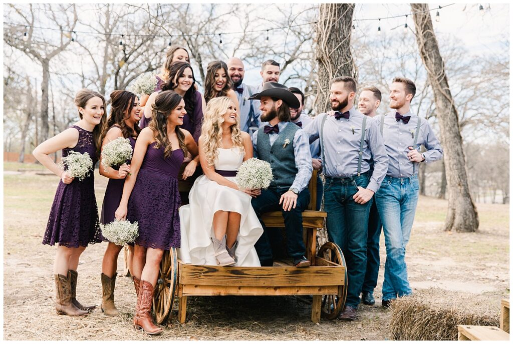 Texas styled bridal party poses with bride and groom on wagon for outdoor Texas styled wedding at Fort Worth Country Memorial Wedding Venue photographed by Dallas wedding photographer Jenny Bui of Picture Bouquet Studio. 