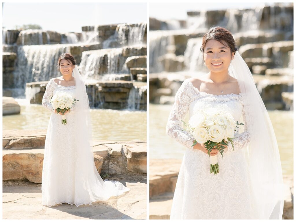 Bride in off shoulder long sleeve lace wedding dress and long veil poses with with white bouquet in front of rock waterfall during bridal party portraits at Flower Mound River Walk photographed by Dallas wedding photographer, Jenny Bui of Picture Bouquet Studio. 