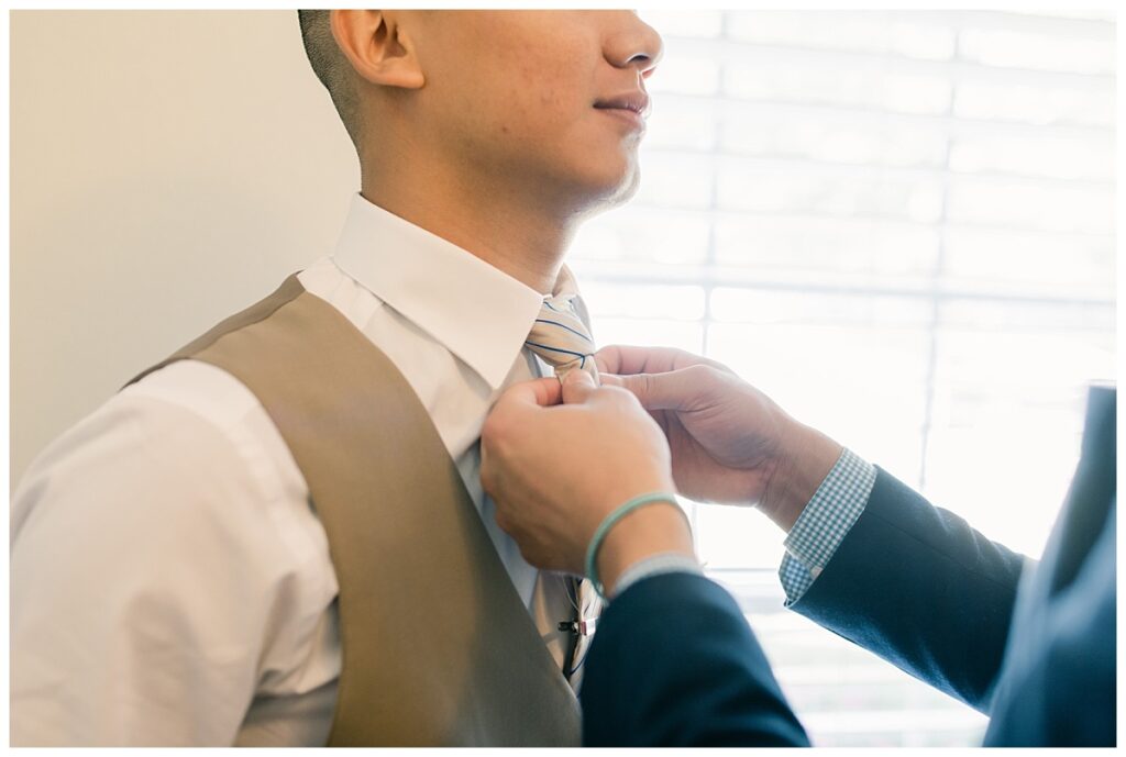 Best man helping groom in tan suit adjust tie during bridal prep photographed by Dallas wedding photographer, Jenny Bui of Picture Bouquet Studio. 