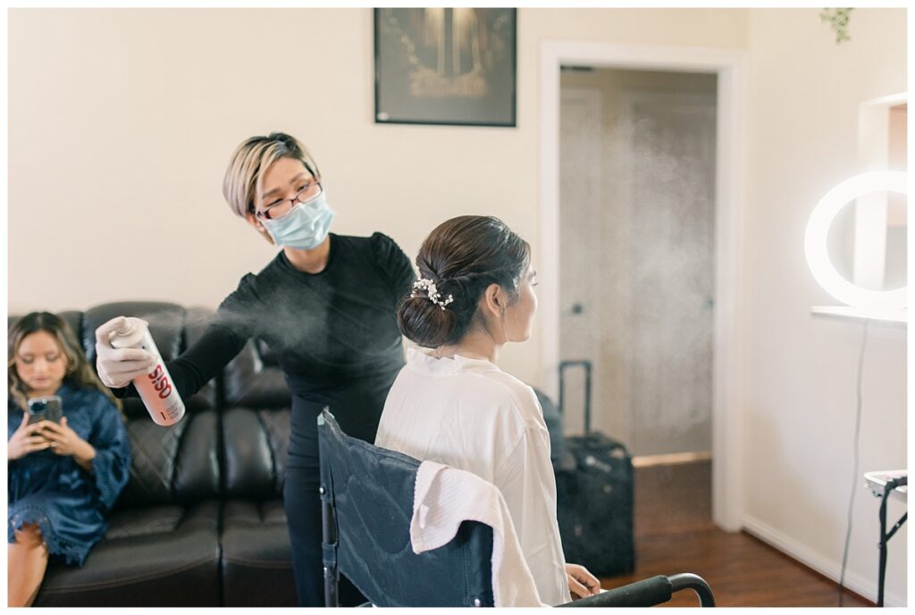 Bride in white silk robe sitting in chair as hairstylist puts finishing touches on bridal hair photographed by Dallas wedding photographer, Jenny Bui of Picture Bouquet Studio. 