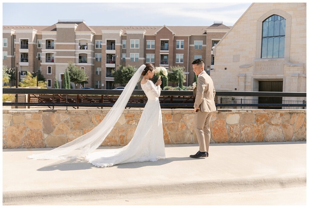 Groom in tan suit turns around for first look of bride in off shoulder white long sleeve lace wedding dress  in front of The Riverwalk Chapel during first look at Flower Mound River Walk photographed by Dallas wedding photographer, Jenny Bui of Picture Bouquet Studio.  