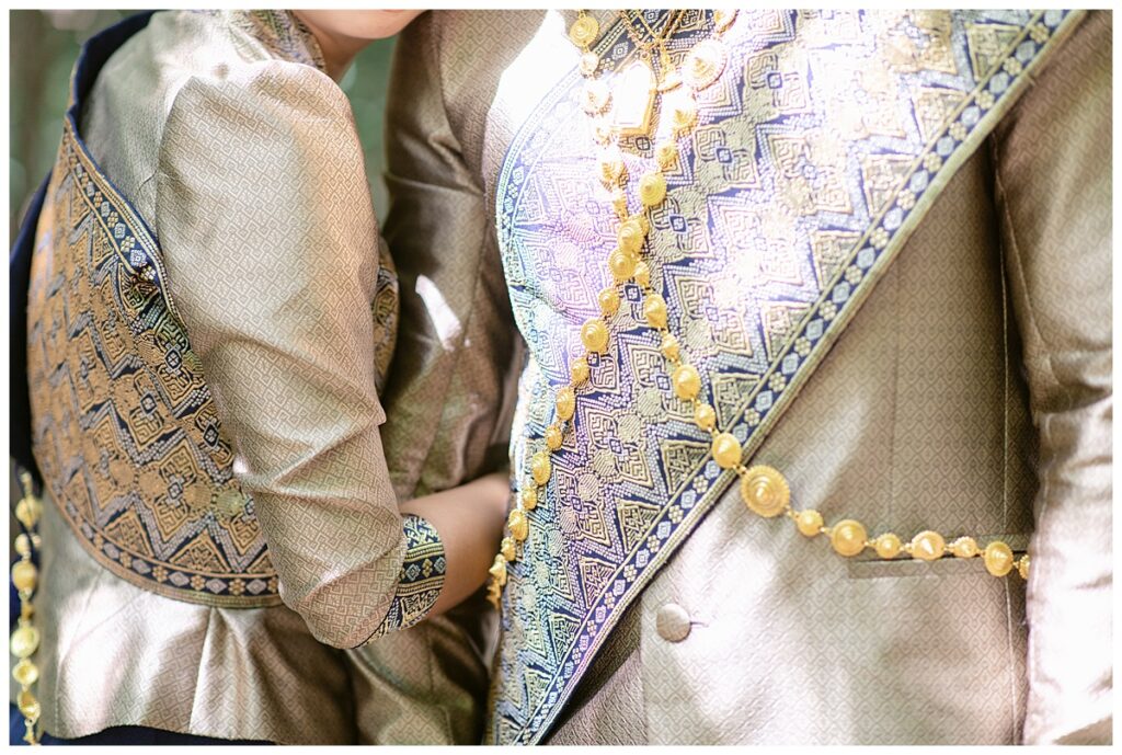 Close up of details of Laotian navy and gold traditional wedding attire on bride and groom for Laotian wedding portrait session at North Richland HIll's park for Jenny Bui of Picture Bouquet Studio, a wedding photography studio serving the Dallas and surrounding areas. 