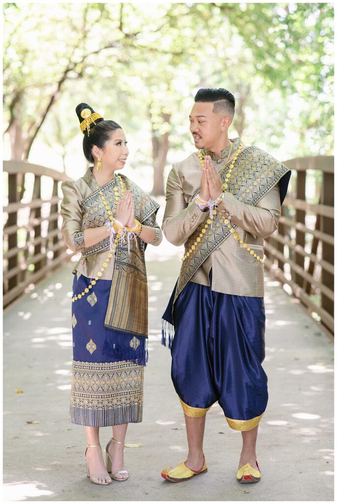 Bride and groom in Laotian navy and gold traditional wedding attire poses  with hands together and looking at each other for Laotian wedding portrait session at North Richland HIll's park for Jenny Bui of Picture Bouquet Studio, a wedding photography studio serving the Dallas and surrounding areas. 