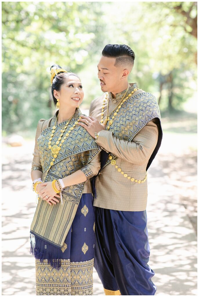 Bride and groom in Laotian navy and gold traditional wedding attire gazes at one another for wedding portrait session at North Richland HIll's park for Jenny Bui of Picture Bouquet Studio, a wedding photography studio serving the Dallas and surrounding areas. 