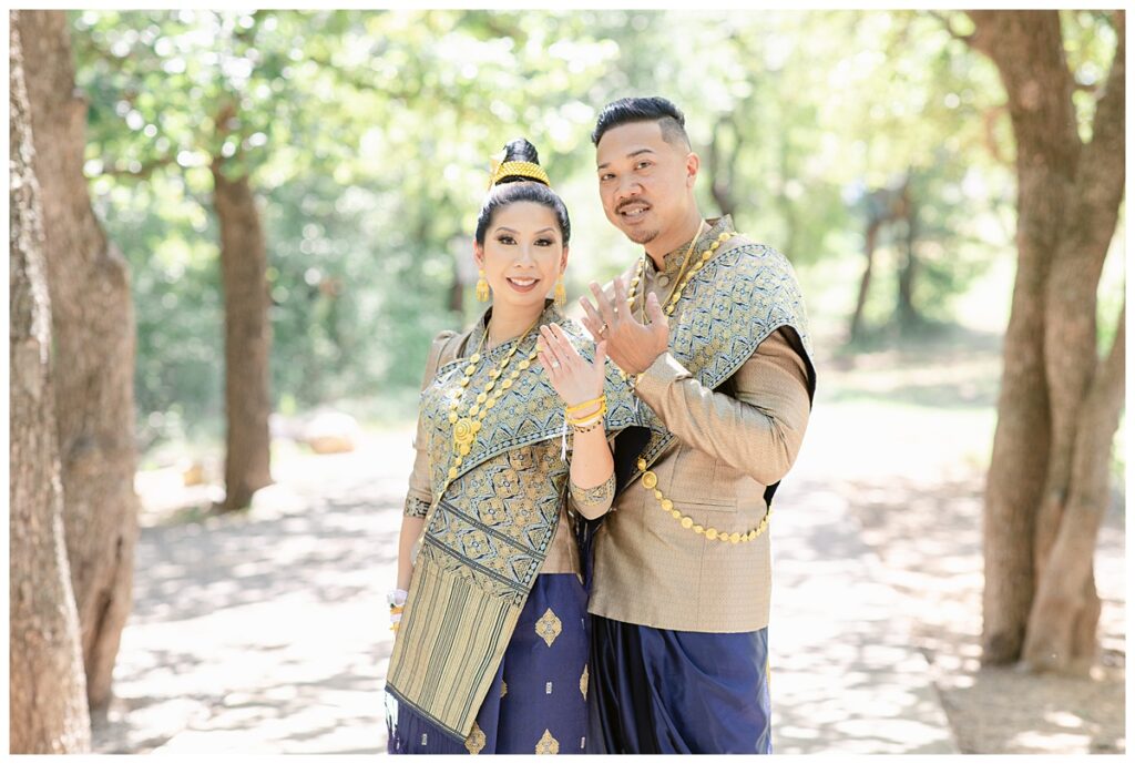 Bride and groom in Laotian navy and gold traditional wedding attire shows off engagement and wedding rings for portrait session at North Richland HIll's park for Jenny Bui of Picture Bouquet Studio, a wedding photography studio serving the Dallas and surrounding areas. 
