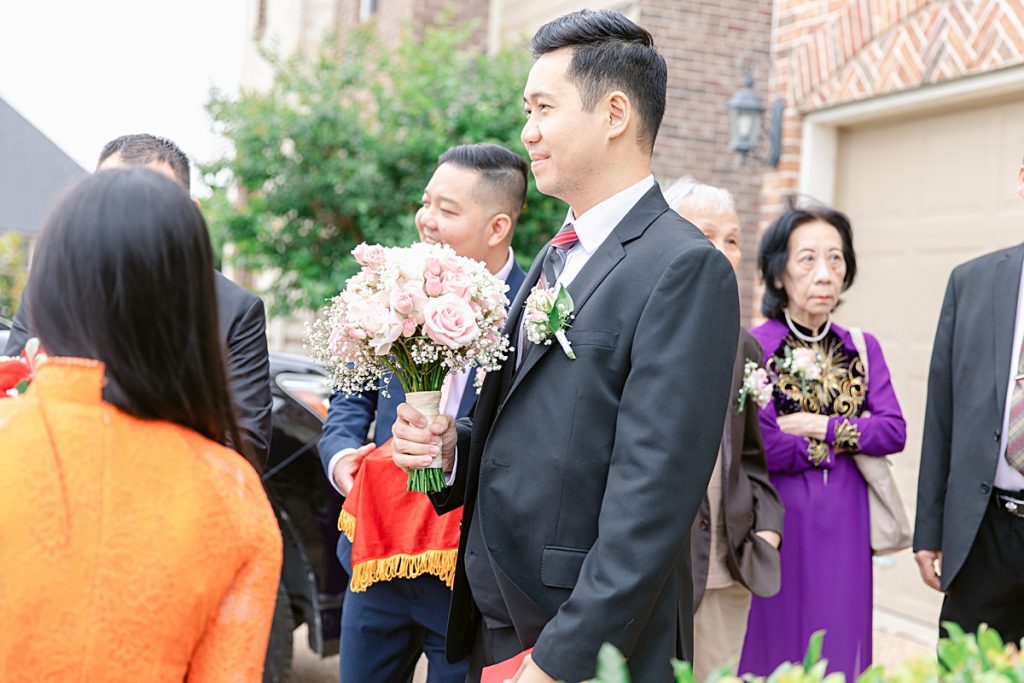 Groom holding bouquet outside bride's home for traditional Vietnamese tea ceremony photographed by Dallas Vietnamese wedding photographer Jenny Bui of Picture Bouquet Studio. 