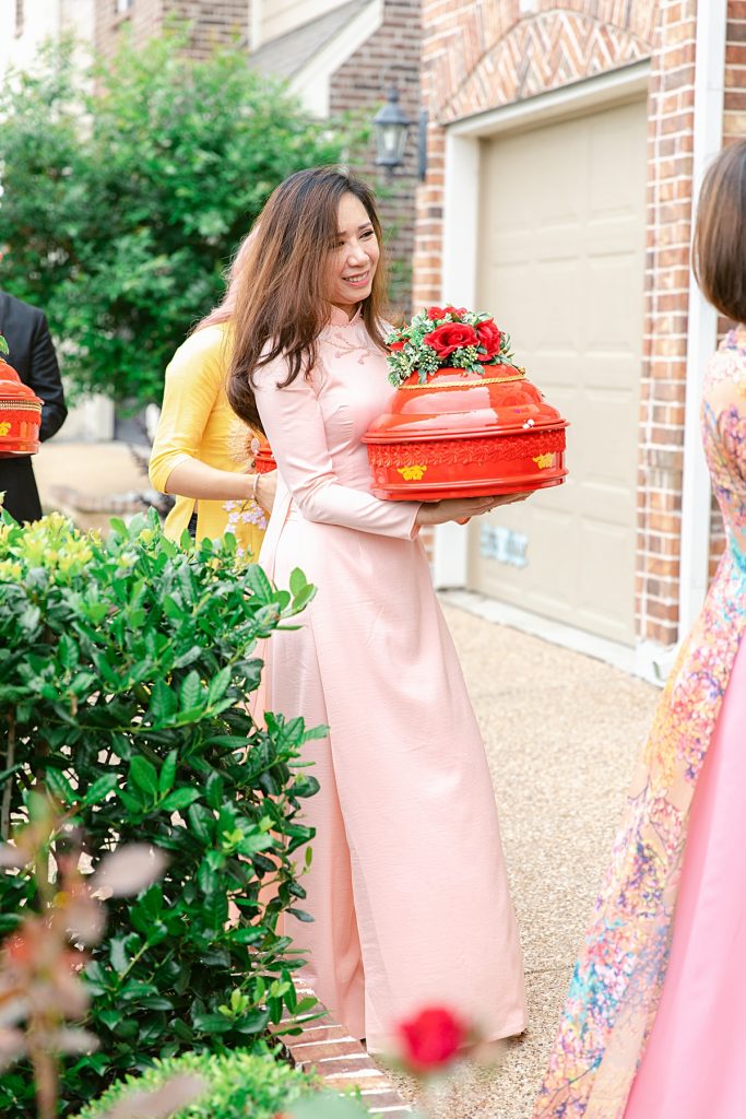 Vietnamese bridesmaid in ao dai carrying red gift tray into bride's home for traditional Vietnamese tea ceremony photographed by Dallas Vietnamese wedding photographer Jenny Bui of Picture Bouquet Studio. 