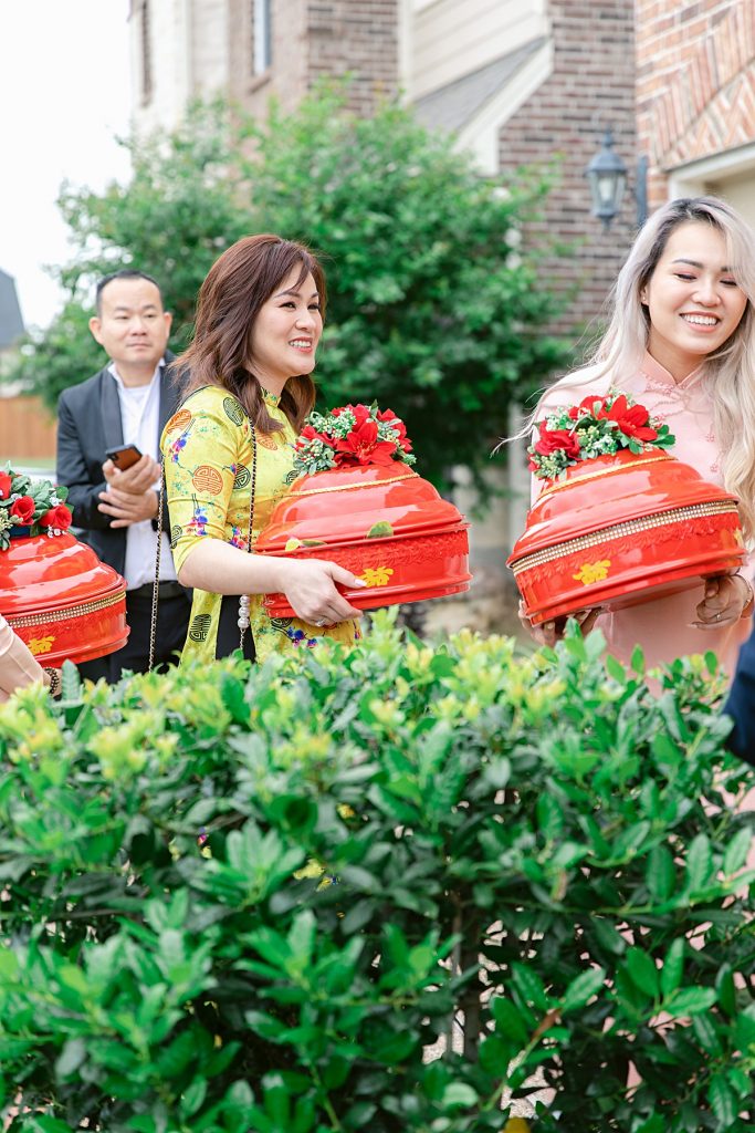 Family members carrying red trays of gifts into the bride's home for traditional Vietnamese tea ceremony photographed by Dallas Vietnamese wedding photographer Jenny Bui of Picture Bouquet Studio. 