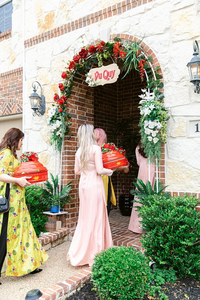 Family member bringing red trays of gifts into the bride's home for traditional Vietnamese tea ceremony photographed by Dallas Vietnamese wedding photographer Jenny Bui of Picture Bouquet Studio. 