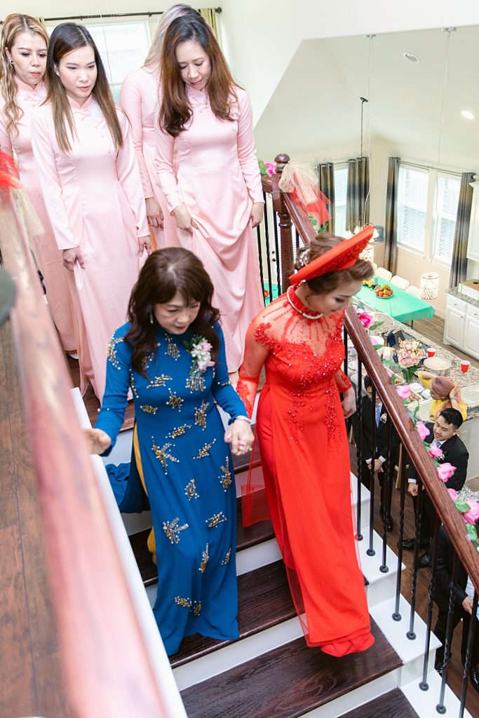 Mother of the Vietnamese bride bringing bride down the stairs followed by bridesmaids in pink ao dai for traditional Vietnamese tea ceremony photographed by Dallas Vietnamese wedding photographer Jenny Bui of Picture Bouquet Studio. 