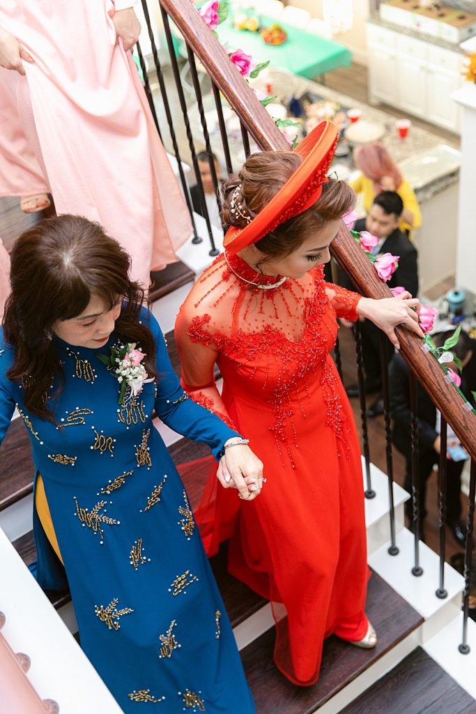 Vietnamese bride in red ao dai coming down the stairs for traditional Vietnamese tea ceremony photographed by Dallas Vietnamese wedding photographer Jenny Bui of Picture Bouquet Studio. 