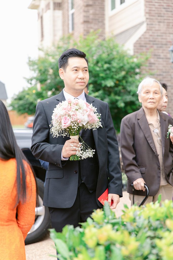 Vietnamese groom holding bouquet outside of bride's home for traditional Vietnamese tea ceremony photographed by Dallas Vietnamese wedding photographer Jenny Bui of Picture Bouquet Studio. 