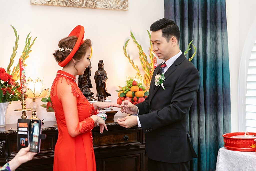 Groom places ring on bride's finger for traditional Vietnamese tea ceremony photographed by Dallas Vietnamese wedding photographer Jenny Bui of Picture Bouquet Studio. 