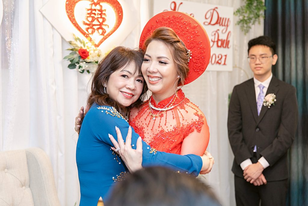Mother of the bride hugging bride for traditional Vietnamese tea ceremony photographed by Dallas Vietnamese wedding photographer Jenny Bui of Picture Bouquet Studio. 