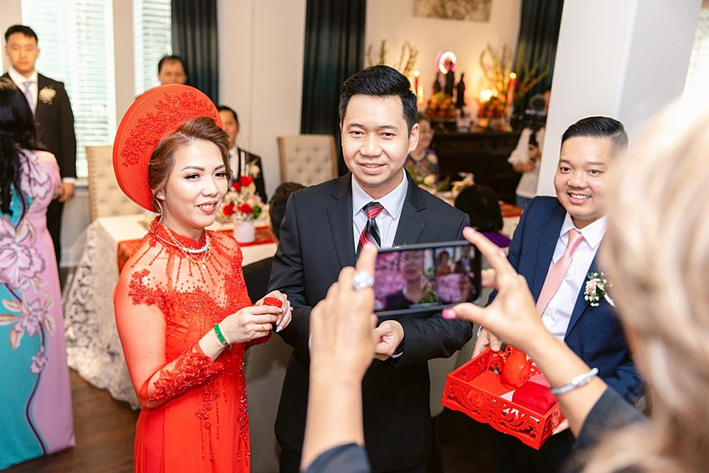 Vietnamese bride and groom presents tea to relatives in Vietnam on video chat for traditional Vietnamese tea ceremony photographed by Dallas Vietnamese wedding photographer Jenny Bui of Picture Bouquet Studio. 