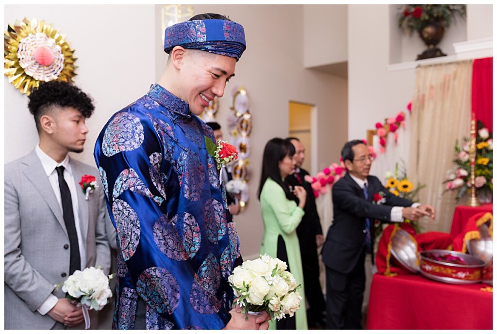 Groom in blue ao dai smiling as traditional Vietnamese tea ceremony begins photographed by Jenny Bui of Picture Bouquet Studio. 