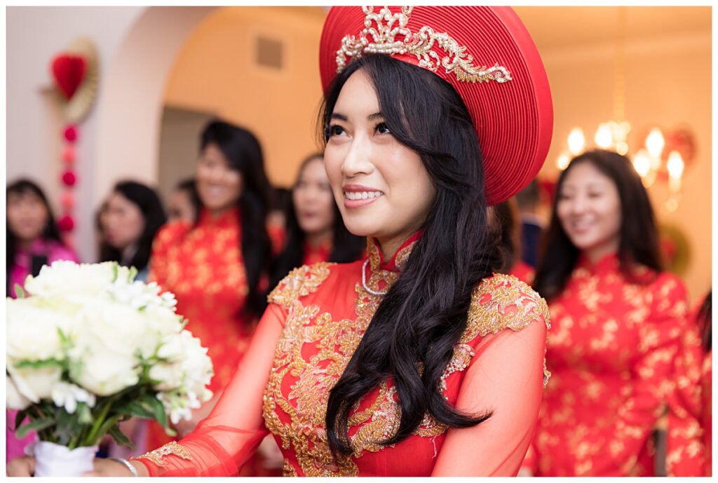 Bride in red ao dai smiling up at groom during traditional Vietnamese tea ceremony photographed by Jenny Bui of Picture Bouquet Studio. 