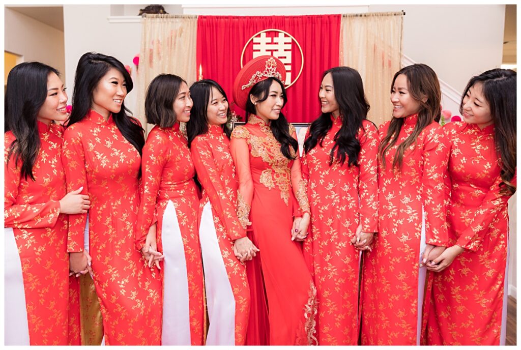 Bride and bridesmaids in red ao dai smiling at each other in front of altar for traditional Vietnamese tea ceremony photographed by Dallas wedding photographer Jenny Bui of Picture Bouquet Studio. 