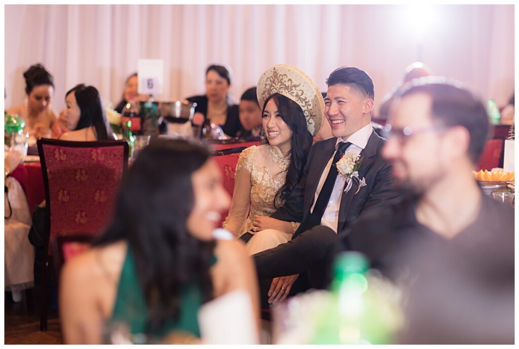 Vietnamese bride in ao dai and groom laughs during speeches for Kirin Court wedding photographed by Dallas Wedding Photographer Jenny Bui of Picture Bouquet Studio. 
