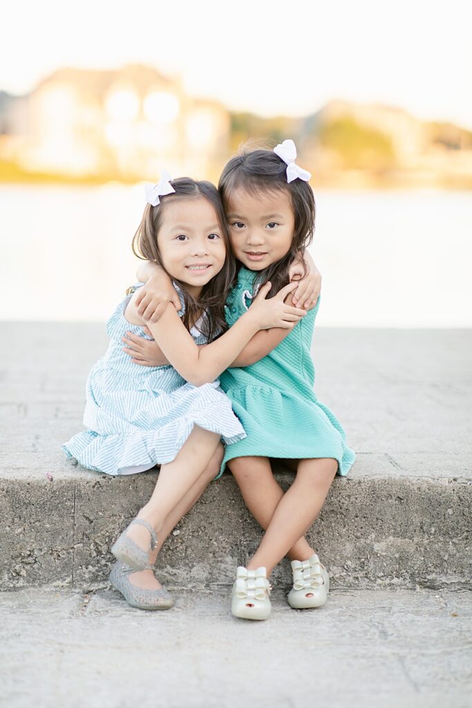 Twin girls in hugging pose at Adriatica Village for family session photographed by Mckinney family photographer Picture Bouquet Studio. 