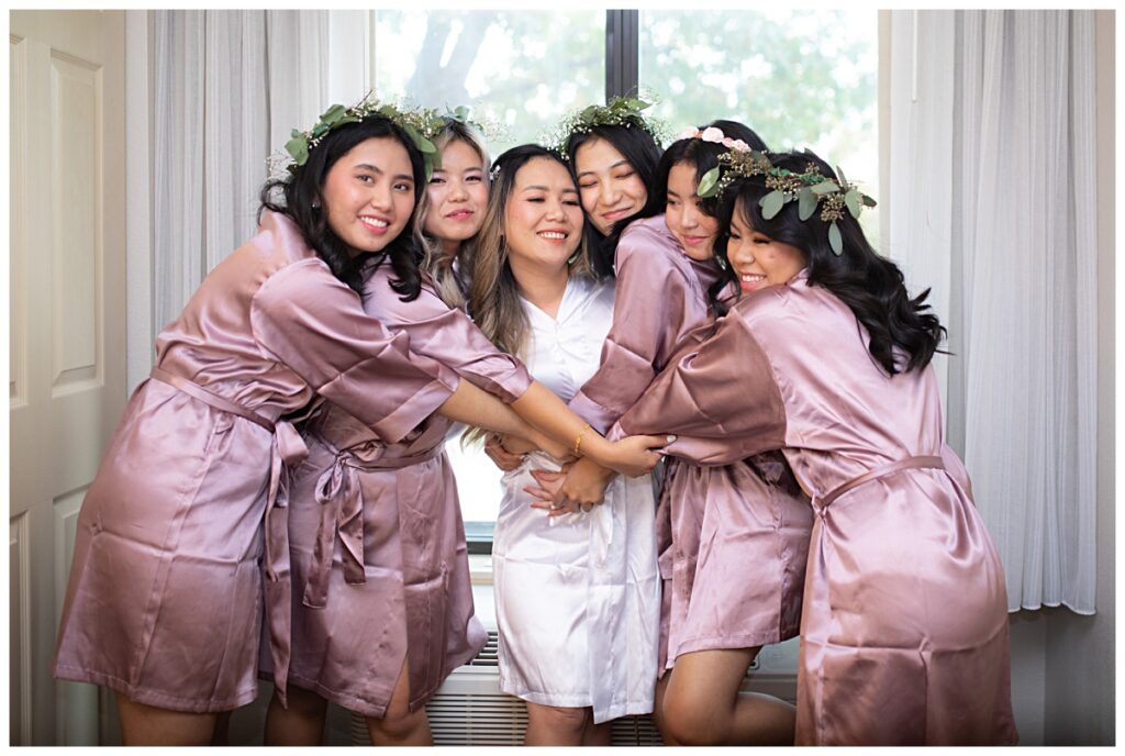Bridesmaids in lavender robes hugging bride in white robe during getting ready for wedding at The Pearl restaurant photographed by Picture Bouquet Studio. 