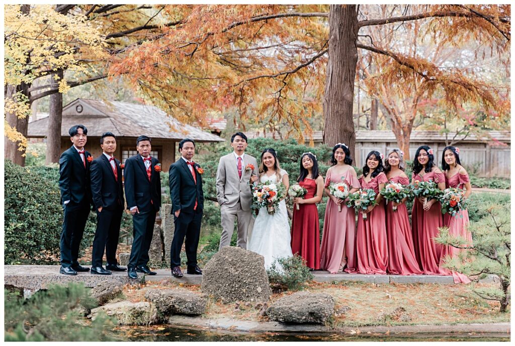 Asian bridal party in dusty and burnt orange fall wedding colors poses at Fort Worth Japanese Garden photographed by Jenny Bui of Picture Bouquet Studio. 