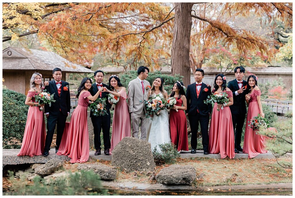 Bridal party in dusty rose and burnt orange poses on bridge at Fort Worth Japanese Garden photographed by Jenny Bui of Picture Bouquet Studio. 