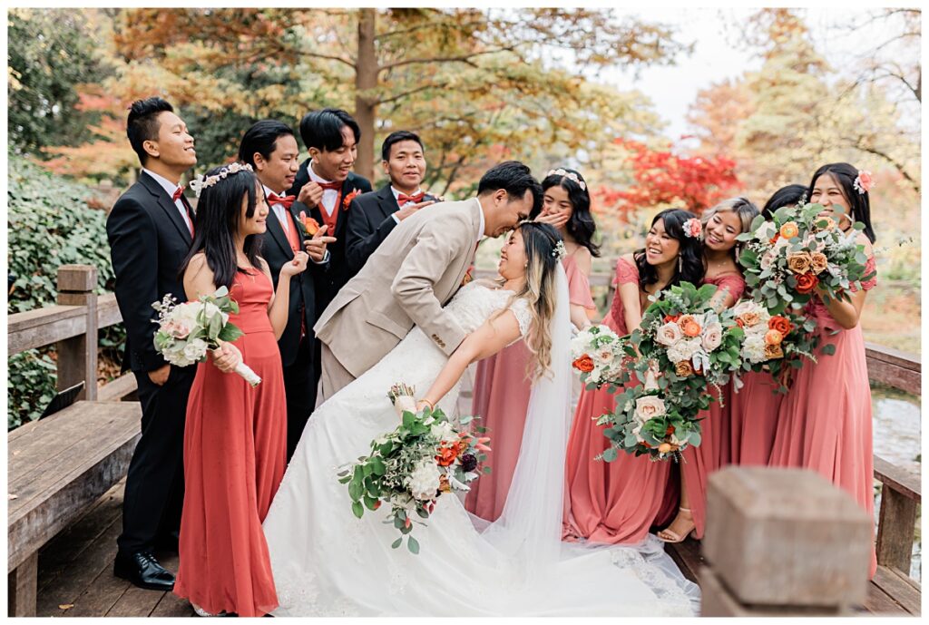 Groom dips bride as bridal party cheers on wooden deck at Fort Worth Japanese Garden photographed by Jenny Bui of Picture Bouquet Studio. 