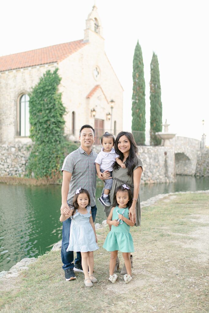 Family of five in pastel green color palette poses in front of Bella Donna Chapel in Adriatica Village for family session photographed by Mckinney family photographer Picture Bouquet Studio. 
