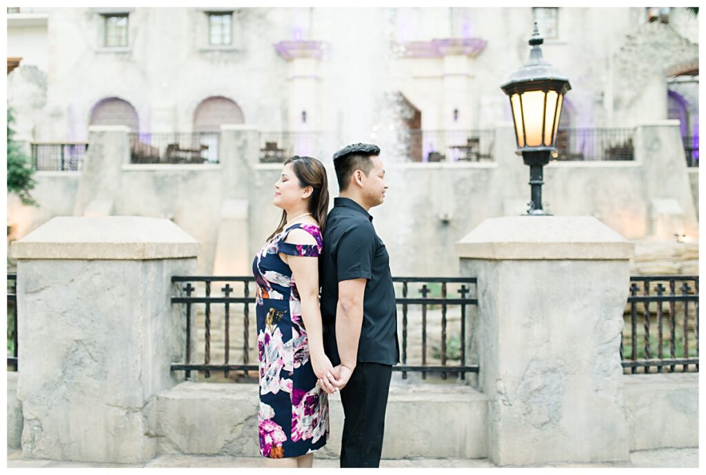 Engaged couple back to back in front of water fountain at Gaylord Texan Resort for engagement session photographed by Picture Bouquet Studio. 