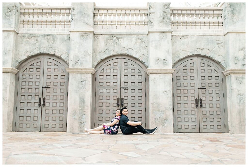 Engaged couple sitting in front of castle door back to back at Gaylord Texan Resort for engagement session photographed by Dallas wedding photographer Jenny Bui of Picture Bouquet Studio. 