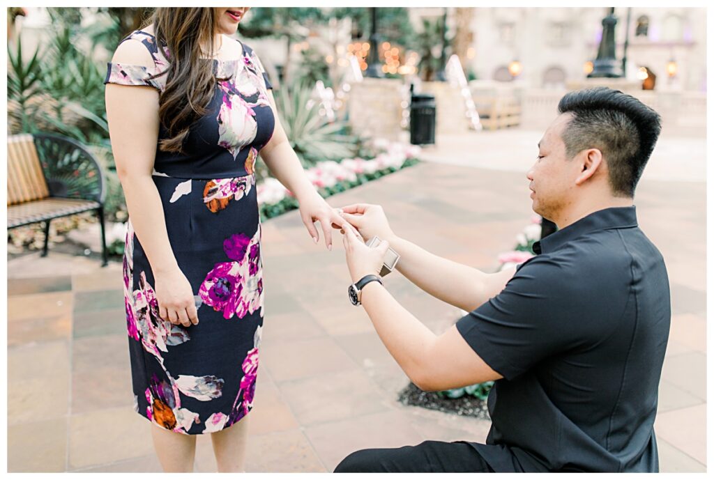 Guy placing diamond ring on fiancee's finger at Gaylord Convention Center for engagement session photographed by Picture Bouquet Studio. 