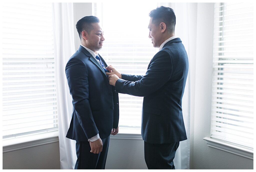 Groom getting tie adjusted during getting ready portion of wedding day for Dallas Vietnamese wedding photographed by Jenny Bui of Picture Bouquet Studio. 