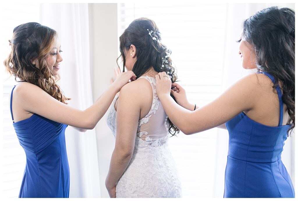 Bridesmaids in royal blue dresses assisting bride get ready on wedding day for Dallas Vietnamese wedding photographed by Jenny Bui of Picture Bouquet Studio. 