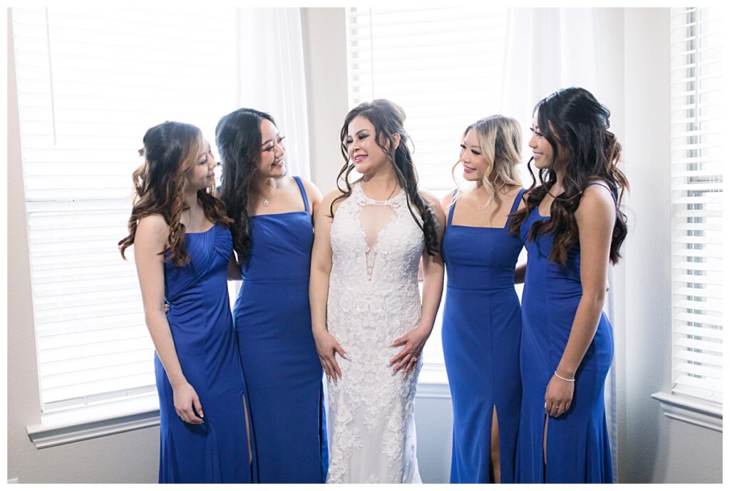 Bride and bridesmaid in floor length royal blue gowns laughs with one another during getting ready portion of wedding day for Dallas Vietnamese wedding photographed by Jenny Bui of Picture Bouquet Studio. 