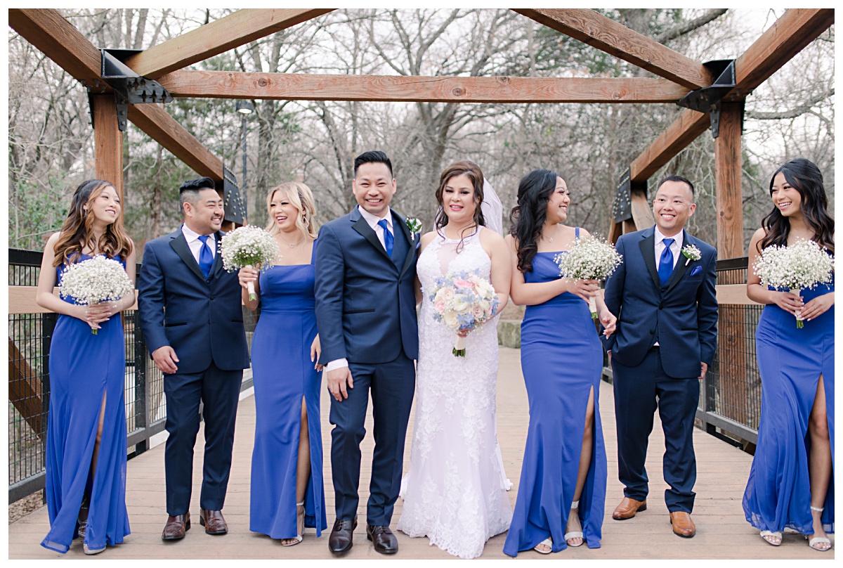 Bridal party in royal blue ensemble laughing as they walk on bridge at Praire Creek Park in Richardson, TX for bridal party photos for Dallas Vietnamese wedding photographed by Jenny Bui of Picture Bouquet Studio. 