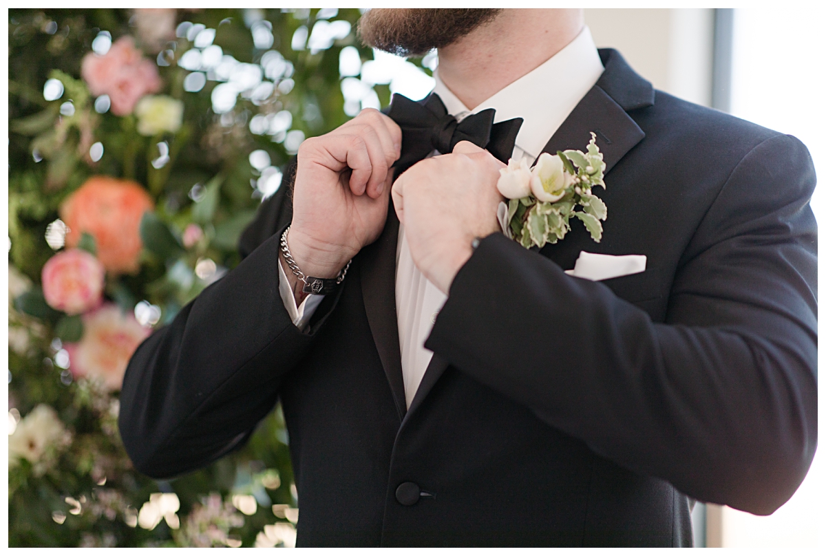 Groom adjusting black bowtie in front of altar  in all white chapel at The Gardenia Venue photographed by Jenny Bui of Picture Bouquet Studio.