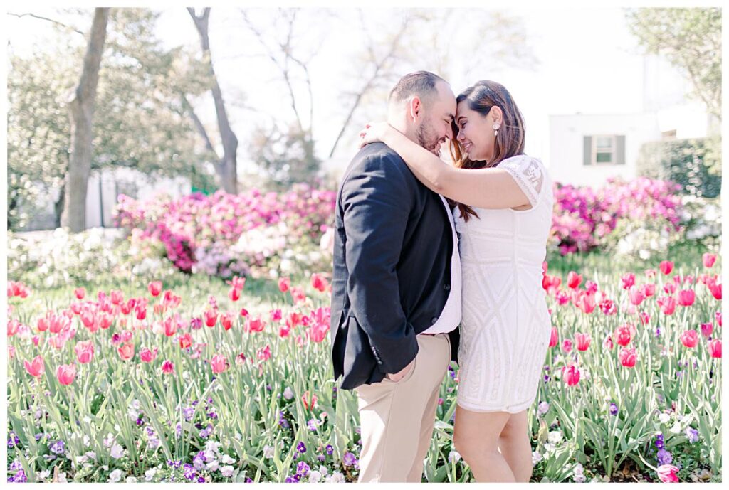 Engaged couple presses forehead together along pink and purple tulip lined pathway at the Dallas Arboretum for their spring engagement session photographed by Jenny Bui of Picture Bouquet Studio. 