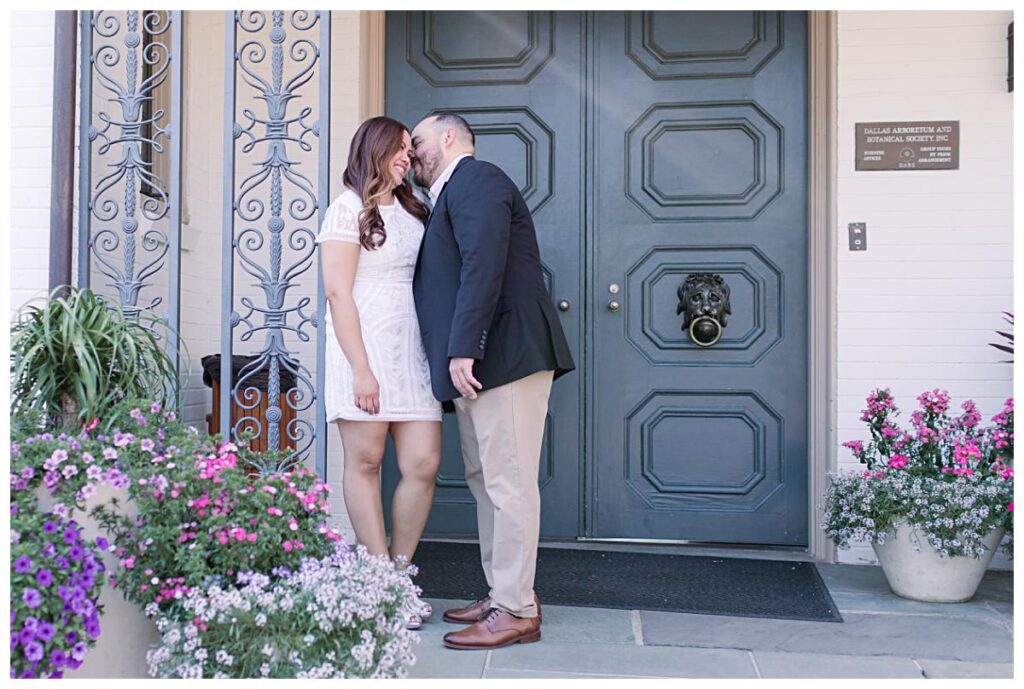 Guy in dressy blazer whispers in fiancee's ears at the Dallas Arboretum for their spring engagement session photographed by Jenny Bui of Picture Bouquet Studio. 