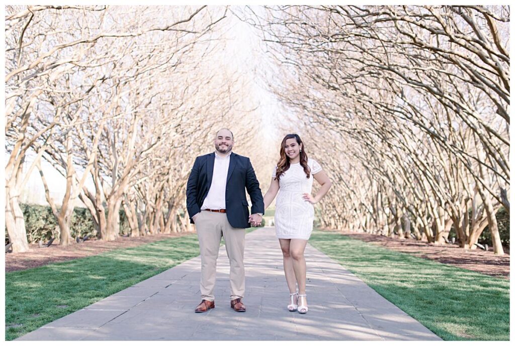 Engaged Dallas couple hold hands underneath the tunnel of crepe myrtle trees at the Dallas Arboretum for their spring engagement session photographed by Jenny Bui of Picture Bouquet Studio. 