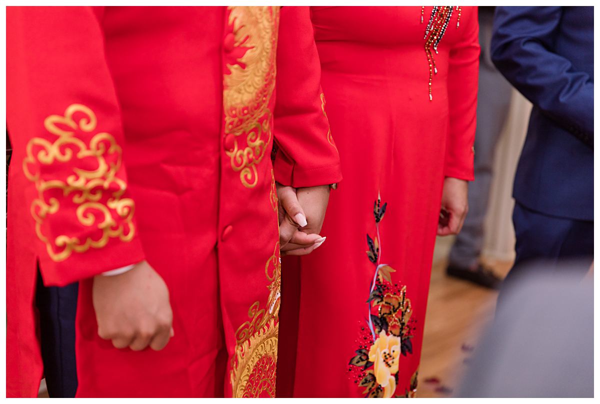 Bride and groom in traditional red ao dai holding hands during Dallas Vietnamese tea ceremony photographed by Jenny Bui of Picture Bouquet Studio. 