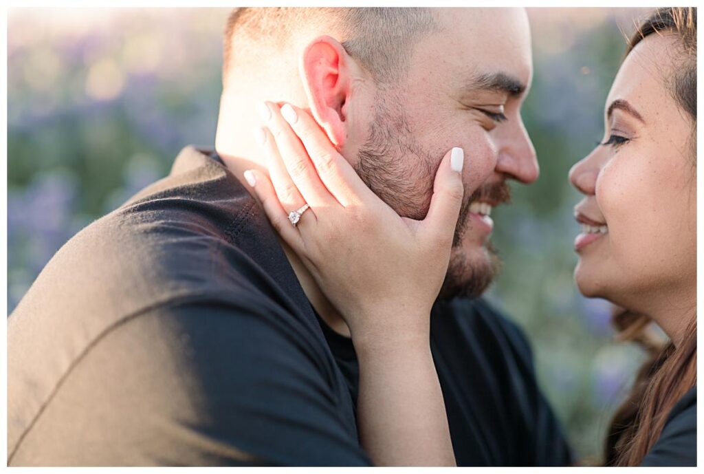 Close up of engagement diamond ring on ring finger as bride-to-be caresses fiance's cheek during Ennis bluebonnet engagement session photographed by Dallas wedding photographer Jenny Bui of Picture Bouquet Studio. 